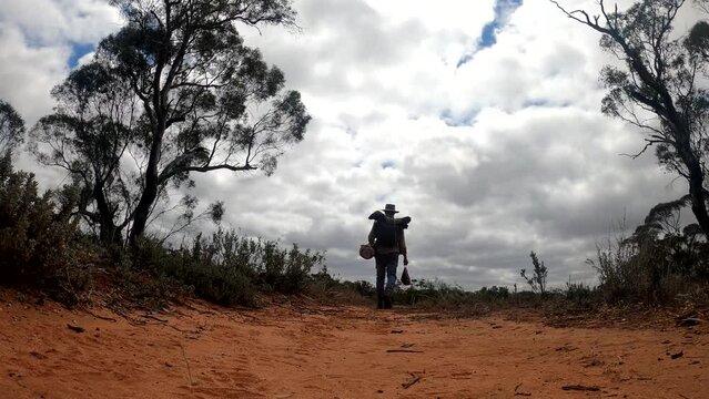 A download shot of an authentic Australian swagman walking on a sandy desert outback track.