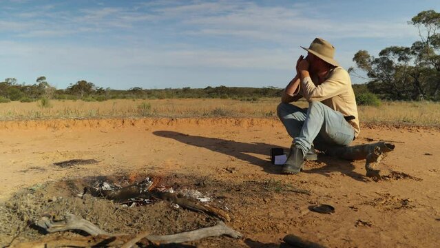 An authentic looking Australian bushman play his harmonica by a campfire in the outback.