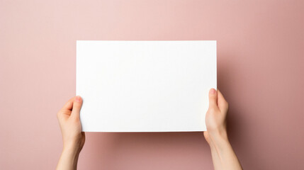 Female hands holding a blank white sheet of paper on a pink background.