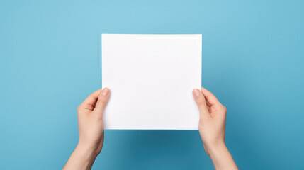 Cropped view of woman holding blank paper sheet isolated on blue background.