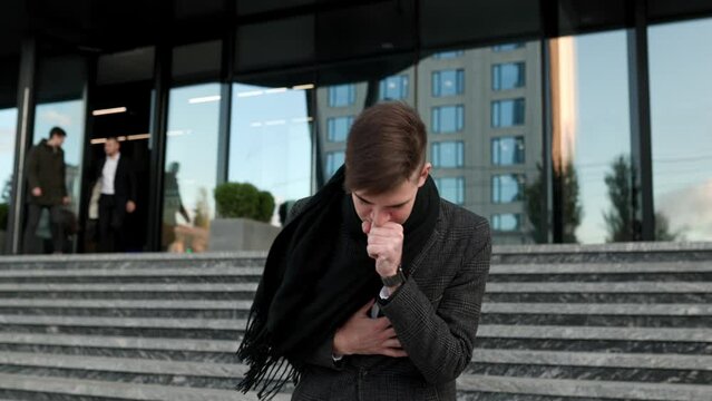Suffering in the City A young man battles the flu with persistent sneezing and coughing, visibly distressed by the seasonal illness while outdoors.