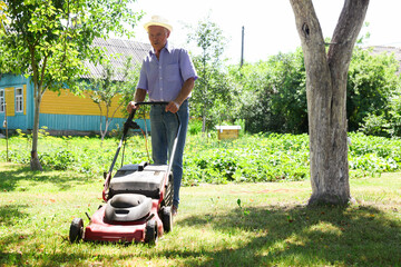 Elderly man with a lawn mower while mowing the lawn