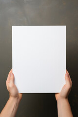 Hands holding blank paper sheet on dark background, top view. Mockup for design.