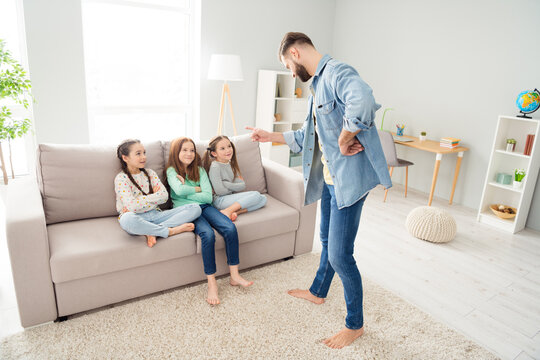 Full size photo of four people guy standing pointing finger cheerful small girls sitting on couch folded arms weekend indoors