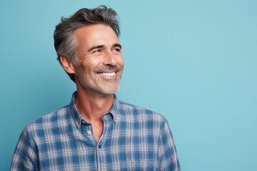 Portrait of a glad man in his 50s wearing a comfy flannel shirt against a pastel blue background. AI Generation