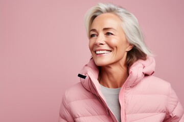 Portrait of a happy woman in her 50s donning a durable down jacket against a pastel pink...