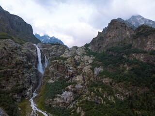 Fototapeta na wymiar Aerial panorama of a Ushbi Waterfall among the Caucasian mountains, Stormy flow of mountain river Dolra. Summer vacation, hiking in Georgia