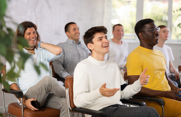 Group of young and middle aged men listening cheerfully to lecture sitting on chairs