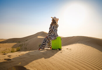 Arabian woman in stylish zebra suit with bright light green or yellow suitcase in sands. Concept...