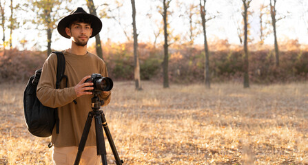 Male professional photographer with camera and tripod in autumn shooting nature