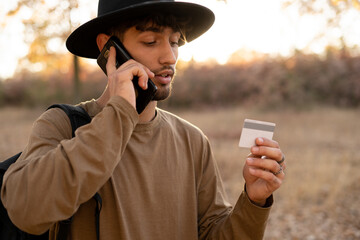 Tourist in autumn forest making online purchases using mobile phone and credit card to pay for order