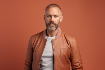 Obraz premium Portrait of a content man in his 40s wearing a trendy bomber jacket against a pastel brown background. AI Generation