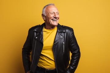 Fototapeta premium Portrait of a smiling man in his 60s sporting a classic leather jacket against a soft yellow background. AI Generation