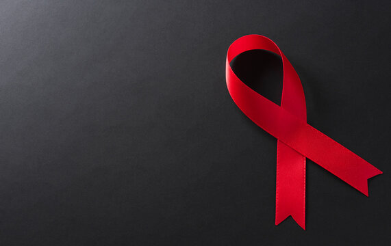 Closeup red ribbon HIV, world AIDS day awareness ribbon on black background. Healthcare and medicine concept.