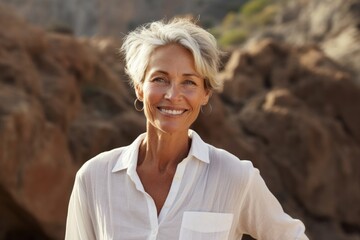 Portrait of a smiling woman in her 60s wearing a simple cotton shirt against a rocky cliff background. AI Generation