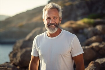 Portrait of a happy man in his 60s dressed in a casual t-shirt against a rocky cliff background. AI...