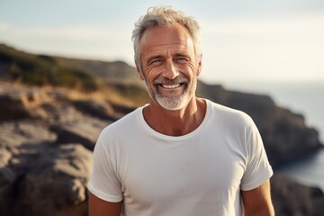 Portrait of a happy man in his 60s dressed in a casual t-shirt against a rocky cliff background. AI...