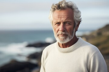 Portrait of a tender man in his 70s wearing a cozy sweater against a serene seaside background. AI Generation