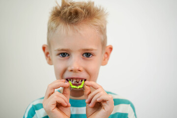 A blond-haired boy inserts orthodontic plate into his mouth to expand jaw and teeth. Close-up. Children's orthodontics, dental treatment, dentistry concept