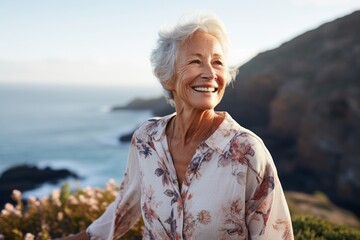 Fototapeta na wymiar Portrait of a happy elderly woman in her 90s dressed in a polished vest against a dramatic coastal cliff background. AI Generation