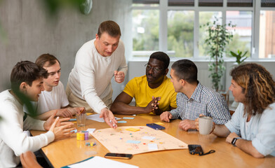 Fototapeta premium Excited man standing on foot playing board game with interested guys sitting around the table