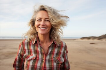 Portrait of a joyful woman in her 50s wearing a comfy flannel shirt against a serene dune landscape background. AI Generation