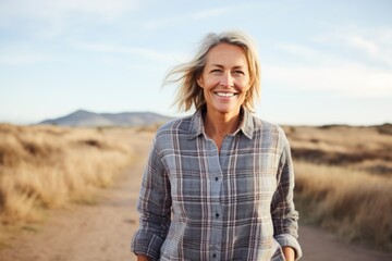 Portrait of a joyful woman in her 50s wearing a comfy flannel shirt against a serene dune landscape background. AI Generation