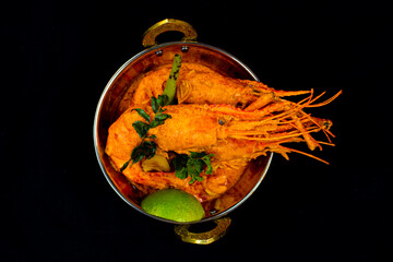 Prawns Curry, lobster curry served in a curry pan on a black background