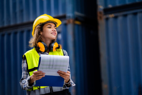 Confident female industrial engineer wearing a white helmet A safety vest works in a cargo logistics center. Freight transport in the container terminal