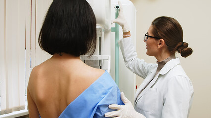 A female doctor in a modern clinic explains the mammography procedure to a topless adult patient undergoing a mammogram. A healthy woman is engaged in cancer prevention in a hospital ward.