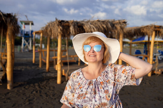 Portrait Of Woman In A Hat And Sunglasses On The Seashore, Cabana With Hanging Beds At The Back