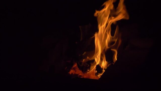 Slow motion. Hot coals in a fire and a bright fire in the complete darkness of the night.