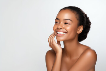 Portrait of a young smiling black woman touching her flawless glowy skin on soft white background, skincare concept