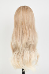 Naklejka premium Natural looking blonde wig on white mannequin head. Long hair on the plastic wig holder isolated on white background, back view.