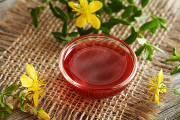 St. John's wort or Hypericum oil in a transparent glass bowl, with fresh flowers