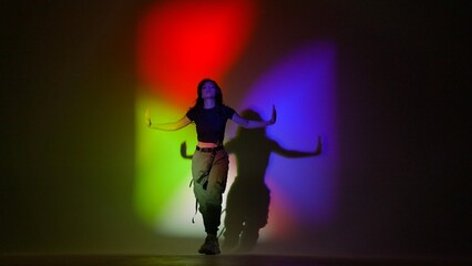 Attractive woman in top and black pants posing at camera dancing jazz funk in studio, isolated on red green blue neon background.