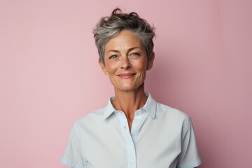 Portrait of a jovial woman in her 50s wearing a simple cotton shirt against a solid pastel color...