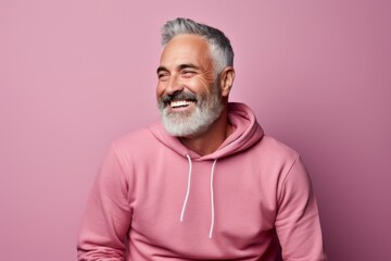 Portrait of a happy man in his 50s sporting a comfortable hoodie against a solid pastel color wall....