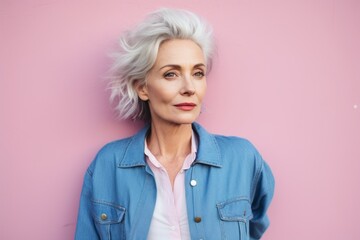 Portrait of a tender woman in her 60s sporting a rugged denim jacket against a solid pastel color...