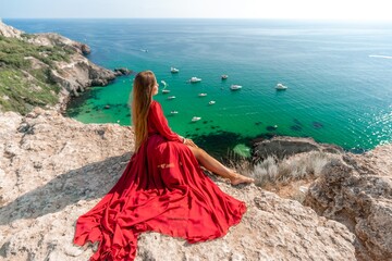 Woman red dress sea. Happy woman in a red dress and white bikini sitting on a rocky outcrop, gazing out at the sea with boats and yachts in the background.