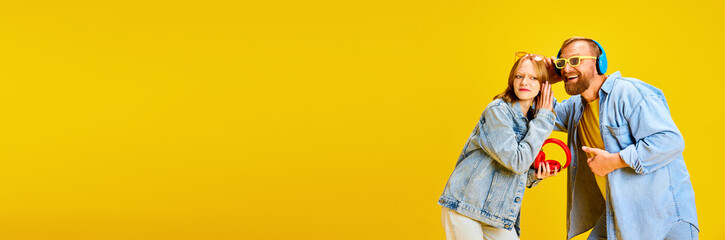 Banner. Father and daughter, parent and kid dressed denim outfit and have fun listening music from one headphones over yellow background.