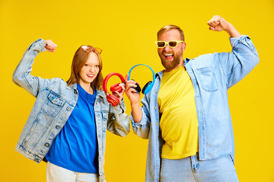 Funny Father And Daughter, Parent And Kid Dressed Style Denim Outfit And Have Fun Holding Headphones Isolated Yellow Studio Background.