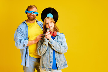 Half length portrait of happy funny father with daughter. Teenager with microphone and dad with headphones and retro music plate isolated yellow background.