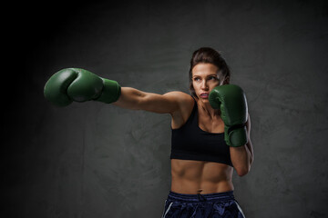 Fit woman boxer in athletic wear, displaying her punch techniques with gloves on, set against a moody background