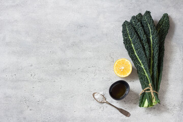 Bunch of black tuscan kale (cavolo nero or lachinato kale), olive oil, lemon and salt on a gray textured background, top view