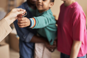 Focus on hands of young real estate agent passing key from new apartment to child held by his...