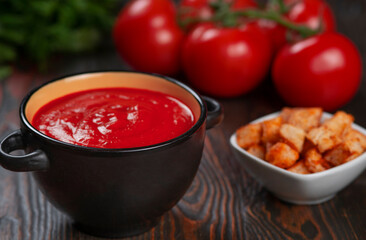 Tomato soup in a black bowl with the inscription Soup on a brown background.