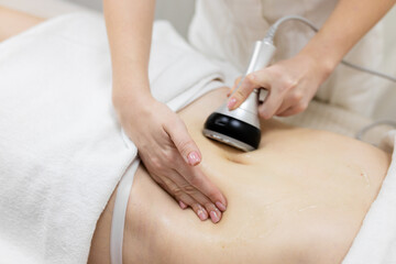 Obraz na płótnie Canvas RF body cavitation lifting procedure in a beauty salon. Ultrasound therapy to reduce fat and elasticity of the skin. Cosmetic ultrasonic anti-cellulite massage close-up
