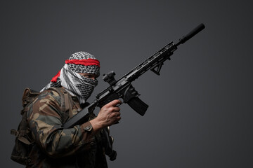 Militant from the Middle East, dressed in a white keffiyeh and camouflaged field attire, wielding an automatic rifle, set against a neutral gray backdrop