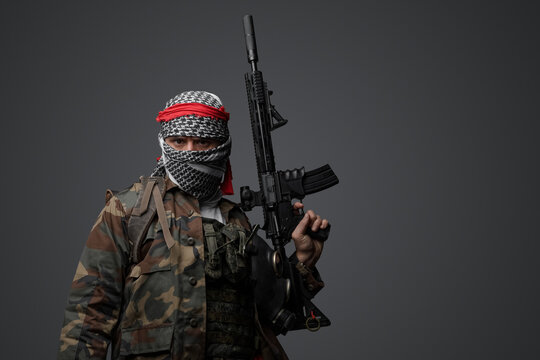 Militant from the Middle East, dressed in a white keffiyeh and camouflaged field attire, wielding an automatic rifle, set against a neutral gray backdrop